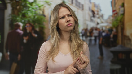 Woman taps index finger against other finger while glancing sideways on a crowded cobblestone street under bright daylight; confusion doubt skepticism.