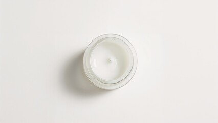 A white candle in a glass container on a white surface.