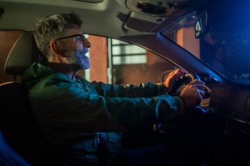 Mature man driving a car at night through urban city streets