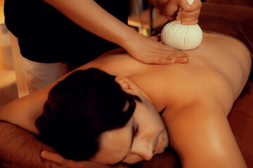 Hot herbal ball spa massage body treatment, masseur gently compresses herb bag on man body....