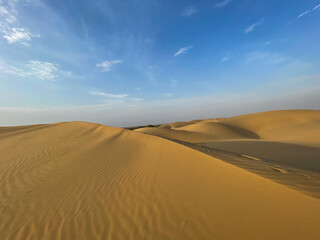 Golden sand dunes of Jaisalmer under a bright blue sky, showcasing the vast and serene Thar Desert landscape with natural patterns and soft evening light.