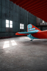 Old aircraft's tail in roomy hangar - pov from under the wing. Empennage of red airplane with blue stripes on rudder and vertical stabilizer.