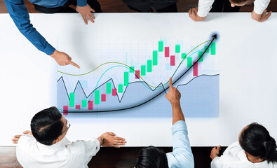A diverse business team examines a financial growth chart on a large screen, analyzing data trends and discussing market performance in a contemporary office setting. Axiom