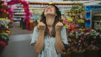 Woman with open mouth and closed eyes raises hands among flowers in a building; happiness celebration.