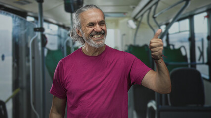 Fototapeta premium Man giving thumbs up and smiling inside a bus, standing near seats and poles in a building transit interior; approval optimism.