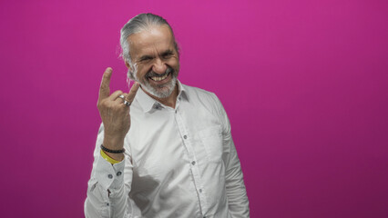 Man with long grey hair and beard showing rock horns with left hand and rings in studio against...