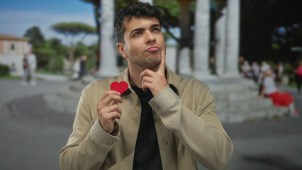 Man holds heart and think about plaza memories while love sparks red paper token by young hispanic travel blogger.