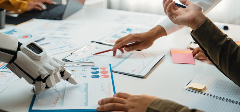 A dynamic scene showing human and robotic hands working together over business charts, exemplifying the fusion of technology and human creativity in the workplace.Noogenesis