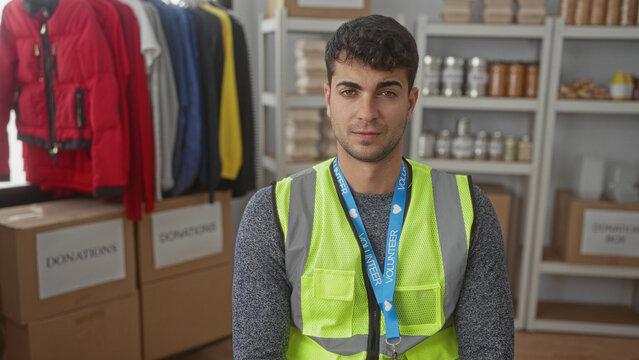 Man with steady face looking around warehouse assists hispanic young volunteer loading donations for charity near another guy.