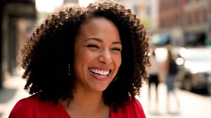A beautiful young woman with curly hair smiles brightly on a sunny city street