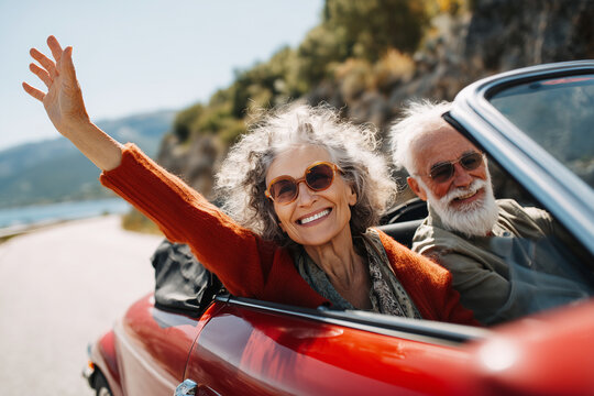 A couple in a red convertible car waving to the camera