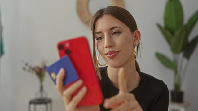 Young woman taps red smartphone and holds blue creditcard in building; convenience security confidence.