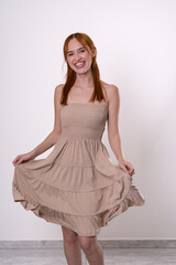 Naklejka premium Red-haired woman smiling while holding dress, minimal and charming studio portrait.