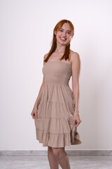 Fototapeta premium Red-haired woman smiling with calm and confident expression, beige dress studio fashion portrait.