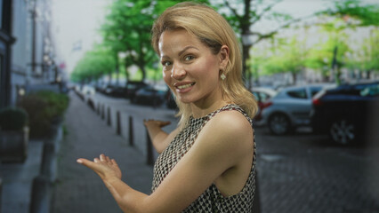 Fototapeta premium Blonde young woman in sleeveless top gestures with open palms toward street; confidence adventure curiosity.