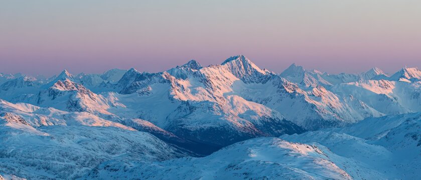A vast, panoramic view of snow-covered mountain peaks at dawn , with alpenglow coloring the tips in soft pink and gold