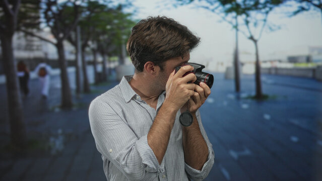 Man adjusting camera with hands and holding lens cap on street while checking settings; curiosity exploration.