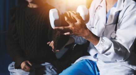 Old woman training with physiotherapist using dumbbells at home. Therapist assisting senior woman with exercises in nursing home. Elderly patient using dumbbells with outstretched arms.