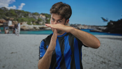 Hispanic man displays hands in time out gesture on beach wearing soccer jersey; youthful determination.