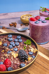 Natural reflections of the morning light capture the dew on the fresh blueberries, enhancing their texture between the smoothie and the cereal on the wooden board