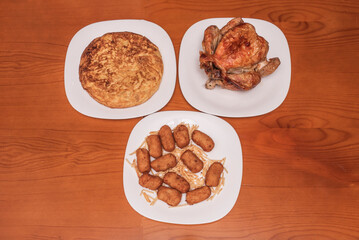 Spanish combination of roast chicken with ham and spinach croquettes, presented on an oval plate with its own juices and lemon wedges for squeezing