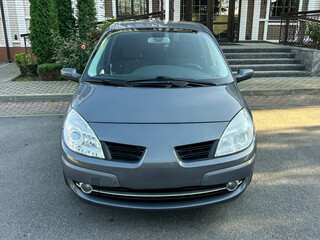 Compact gray car parked gracefully outside a stylish building with green hedges and neat stone pathways in the afternoon sun