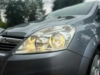 Close-up view of a sleek gray car's headlight highlighting its modern design during a cloudy...