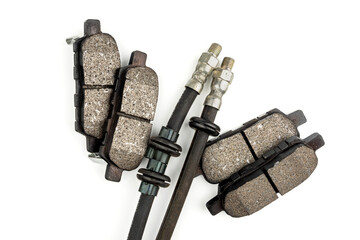 Close-up of new front car brake pads with dark gray friction material and metal backing. Front brake hoses. White background.