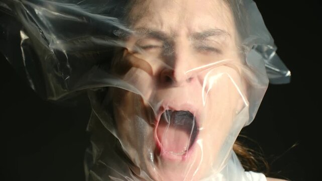 suffocation near film, actress faces plastic wrap struggle, intense scene of woman bound by plastic, dramatic portrayal of woman trapped under plastic with tense facial expressions and dramatic