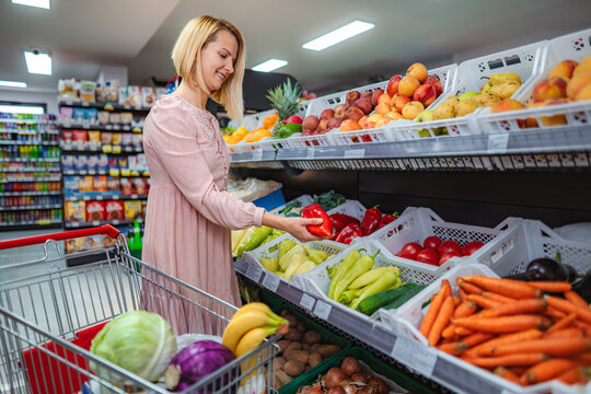 Woman shopping for fresh red pepper in supermarket produce section