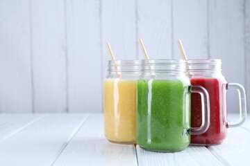 Different tasty smoothies in mason jars on white wooden table