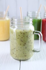 Different tasty smoothies in mason jars on white wooden table
