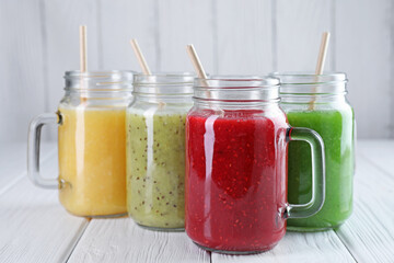 Different tasty smoothies in mason jars on white wooden table