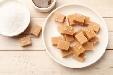 Tasty candies, salt and caramel sauce on light wooden table, flat lay