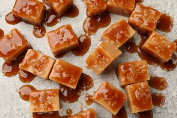 Tasty candies with salt and caramel sauce on grey textured table, flat lay