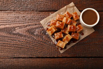 Tasty candies with salt and caramel sauce on wooden table, top view. Space for text