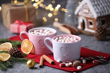 Tasty cocoa with marshmallows, cinnamon and Christmas decor on grey table against blurred lights, closeup