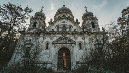 Abandoned church with domes and crosses, surrounded by trees, in a state of decay and neglect.
