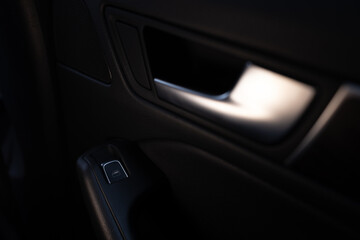 Close-up of a modern car's door panel with chrome handle and window control button. Dark, moody,...