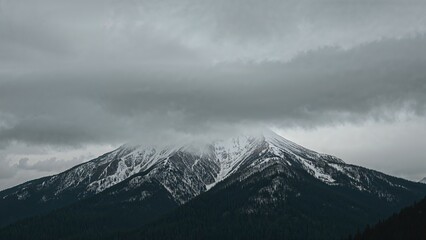 Snow-capped mountain under cloudy sky with swirling clouds overhead. Nature and landscape scene. The mountain's peak obscured by thick weather conditions.