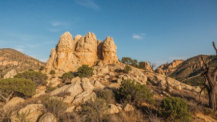 Fototapeta premium Rock formations in a desert landscape with scattered shrubs and a clear blue sky.