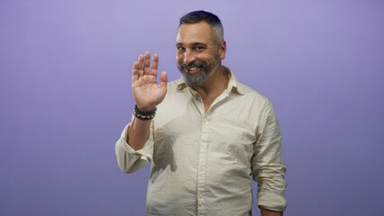 Middle aged hispanic man with salt and pepper beard smiling in purple studio wearing beige linen shirt and rolled sleeves; friendly confidence.