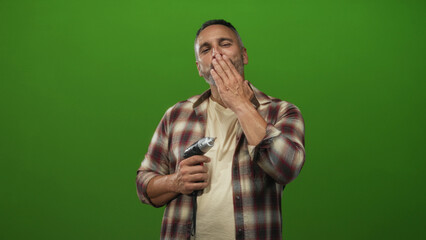 Man carpenter holding power drill, right hand visible on tool, smiling, middle aged with grey hair and beard in green studio; friendly confidence.