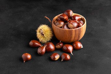 Fresh chestnuts in a rustic wooden bowl set on black background, creating a warm autumn kitchen mood