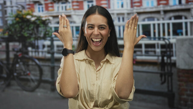 Woman with hands covering face and sticking tongue out on street in amsterdam canal district; playful spontaneous gesture. - Powered by Adobe