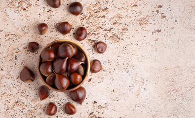 Fresh chestnuts displayed in a wooden bowl and on beige background with copy space, banner simple and clean composition