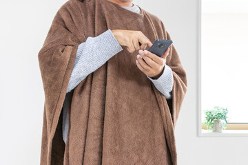 着る毛布を着てスマートフォンを使う男性（30代、日本人、顔無し）