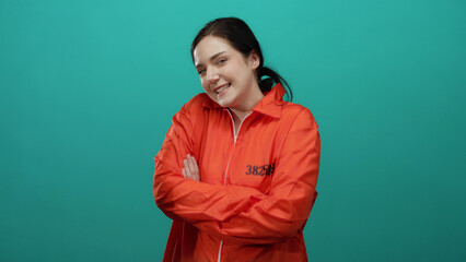 Woman smiling in orange prison jumpsuit with arms crossed against a green background, showcasing a confident and lighthearted attitude.