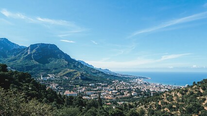 Obraz premium Mountain landscape with a city, coast, and sea under clear blue sky. Urban and natural scenery, coastal view, and greenery.