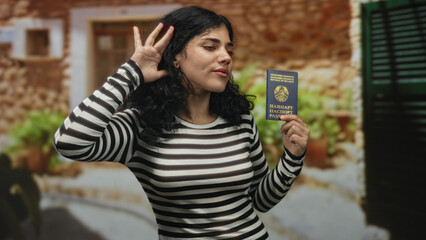 Young woman holding a belarus passport and raising her hand at a building entrance, striped top...